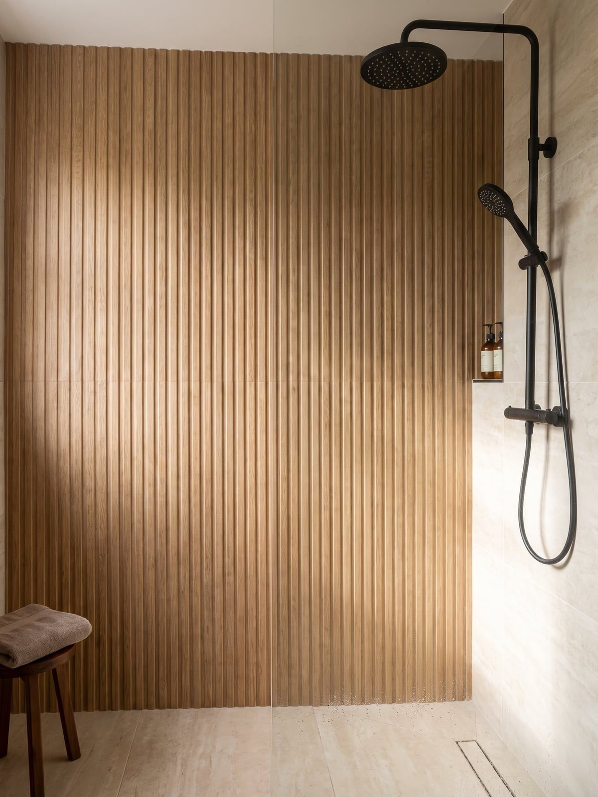 Shower area with a fluted oak-effect wall, a matt black rain shower on a riser rail and a handset on a slide rail