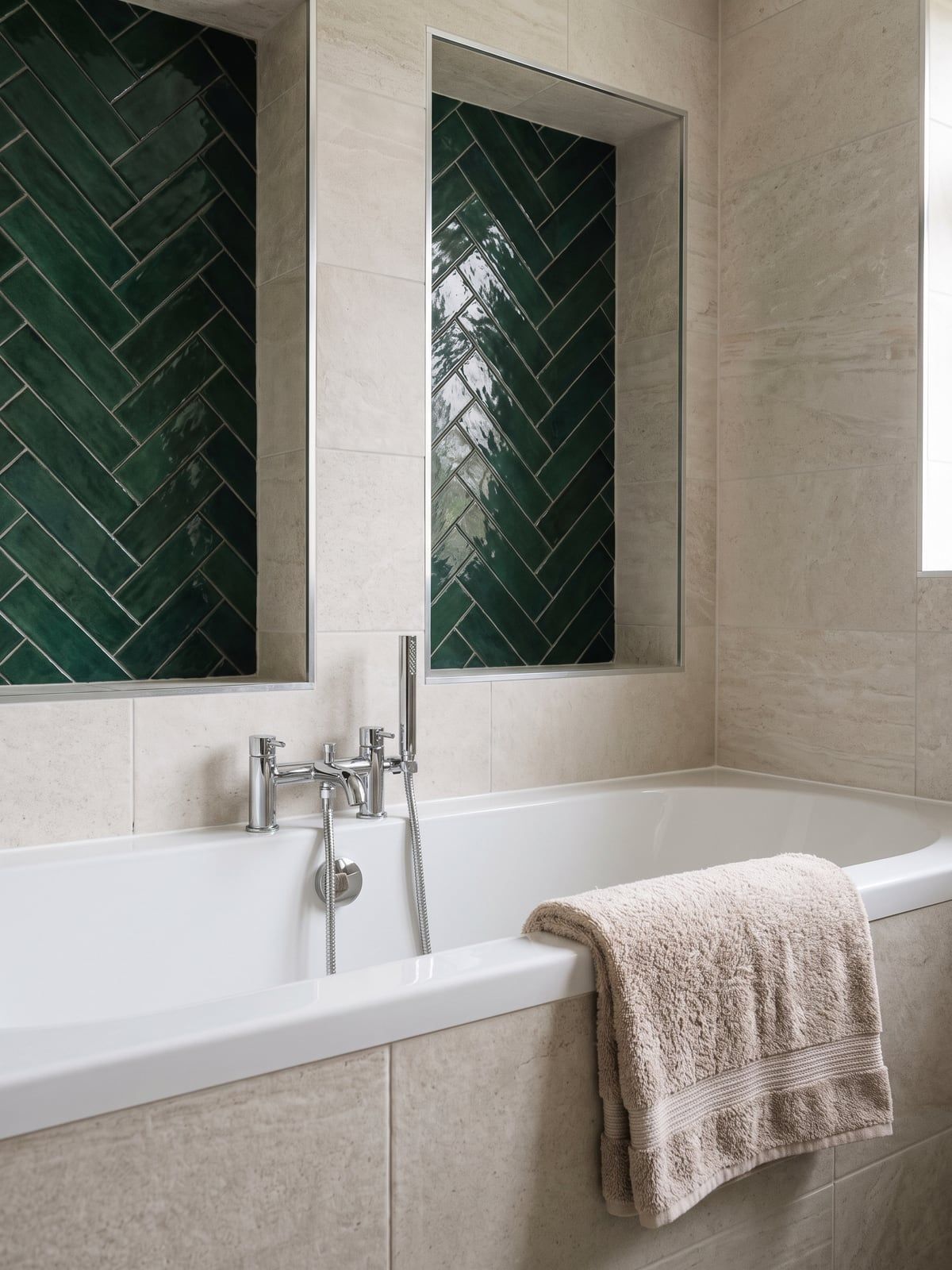 White bath with a chrome filler and handset, with two recesses lined in green herringbone tile behind it