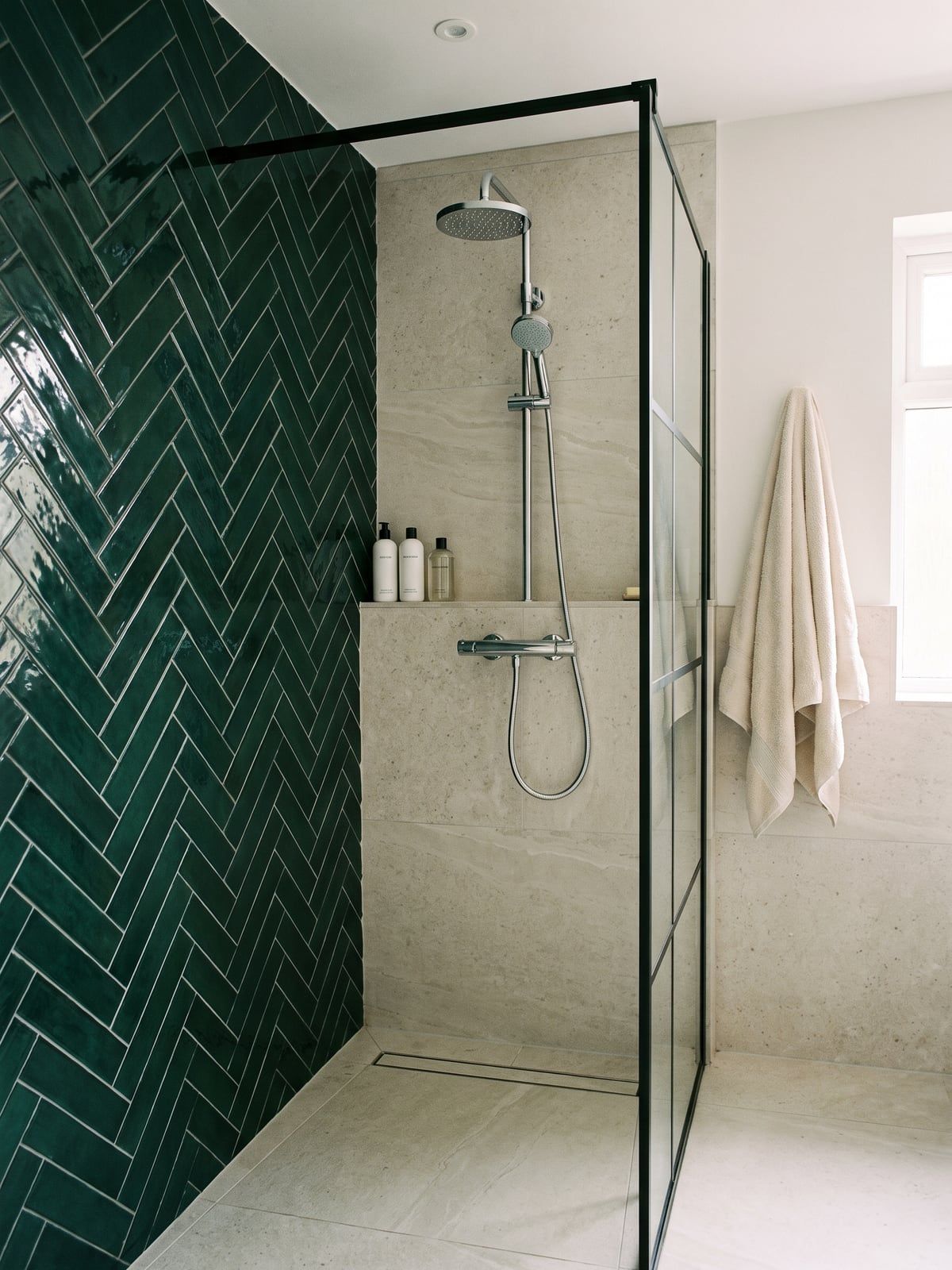 Shower with green herringbone tile on the side wall, a chrome shower set on the pale wall and a linear drain in the floor