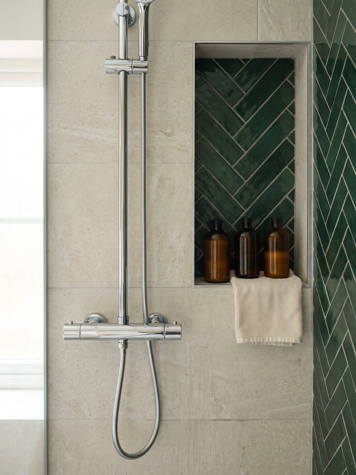 Chrome shower set on the pale wall of the shower, with the green herringbone tile alongside and a recess in the wall