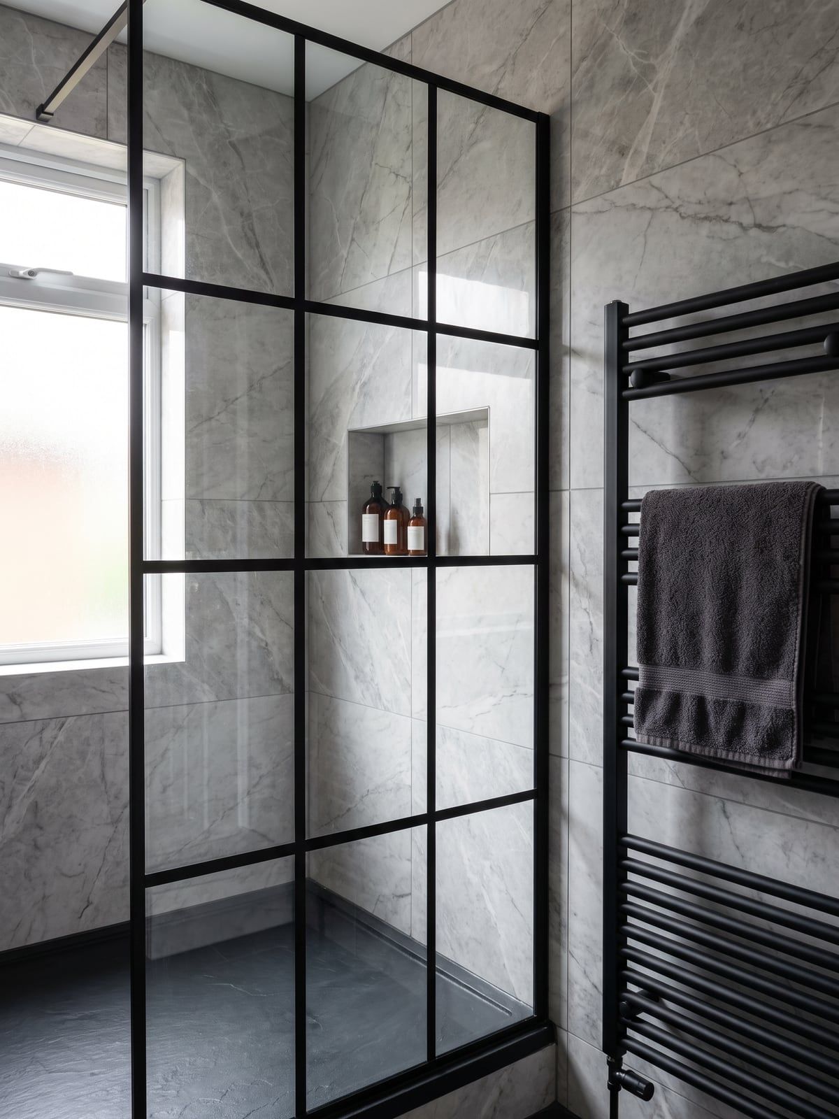 Shower with a black steel-framed screen in a grid of panes, a matt black towel radiator and grey marble-effect tiles