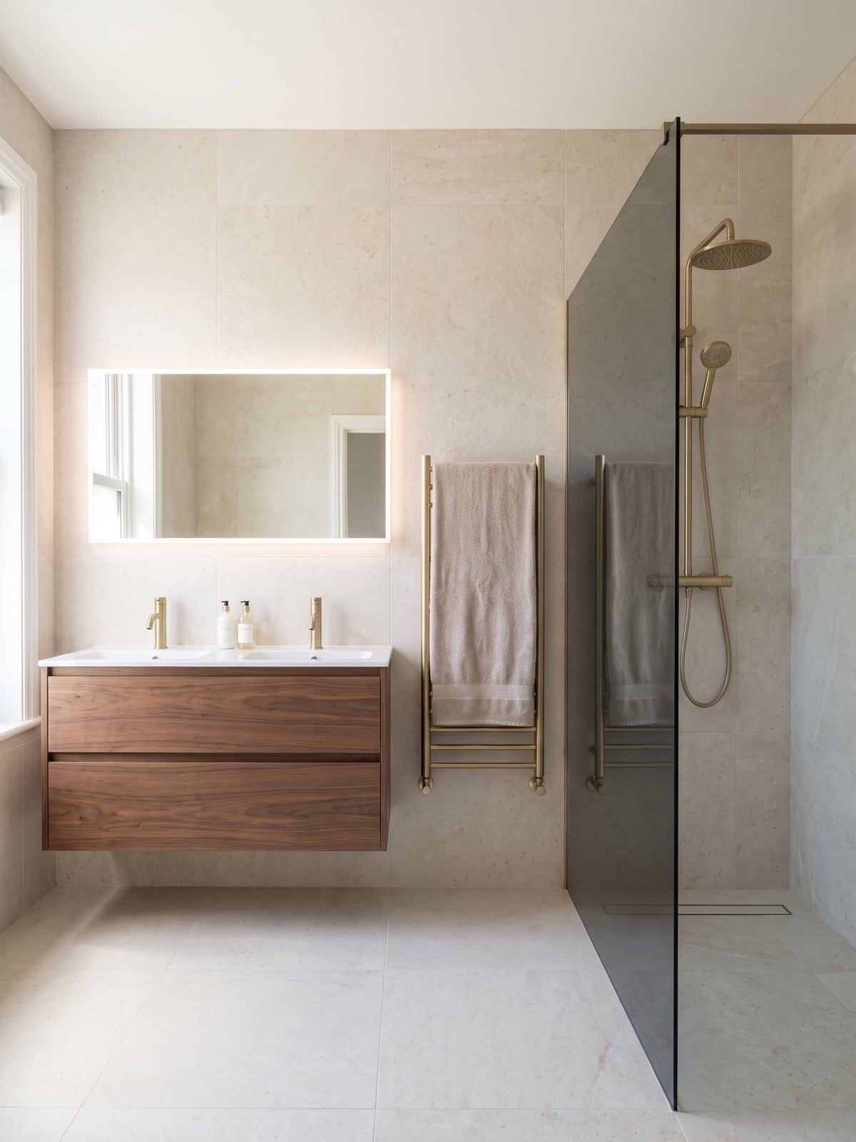 Vanity unit with a backlit mirror beside a walk-in shower with a smoked glass screen and a brushed brass rain shower