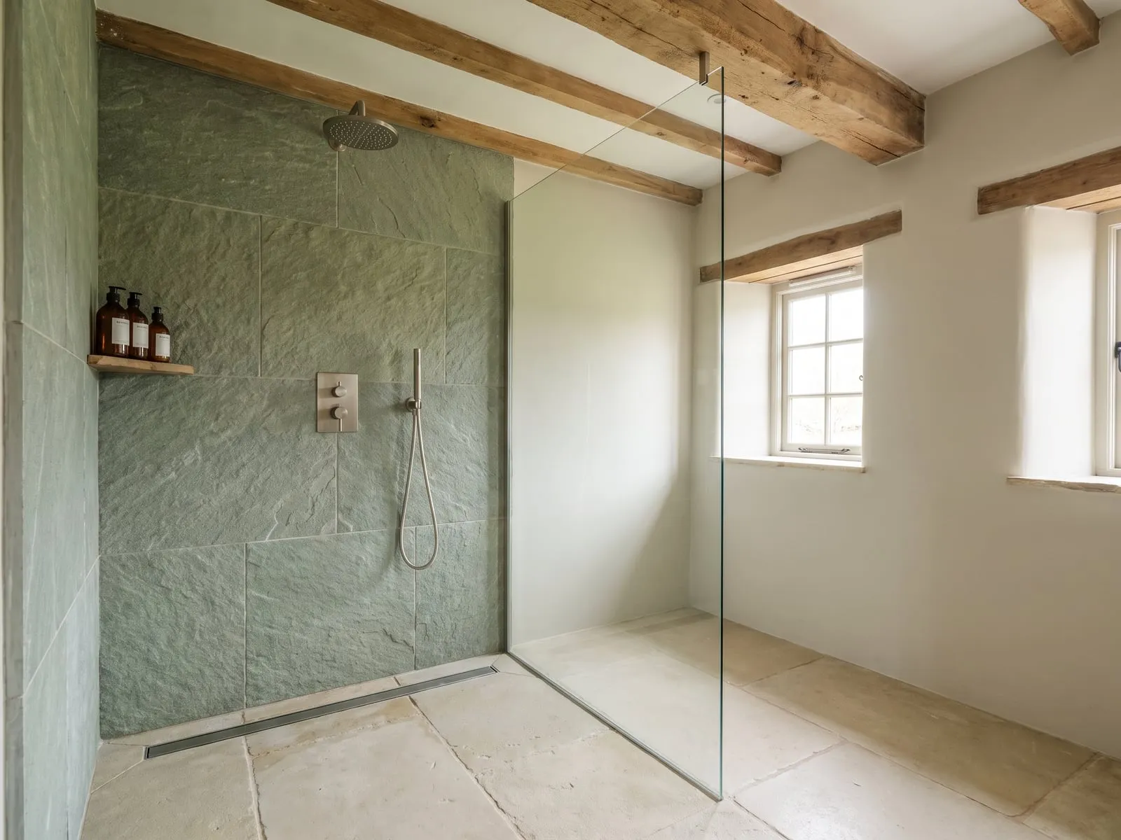 A linear drain set into the floor of a walk-in shower with green natural stone tiles