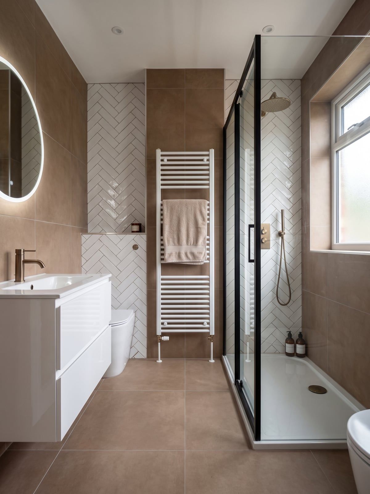 Bathroom with a white gloss vanity unit, a brushed bronze tap, a tall white towel radiator and a black-framed shower enclosure