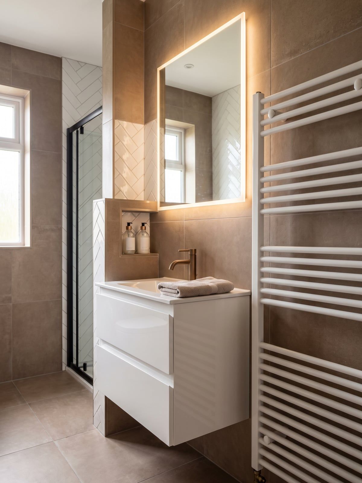 White gloss vanity unit with a brushed bronze tap and a backlit mirror above, beside a tall white towel radiator