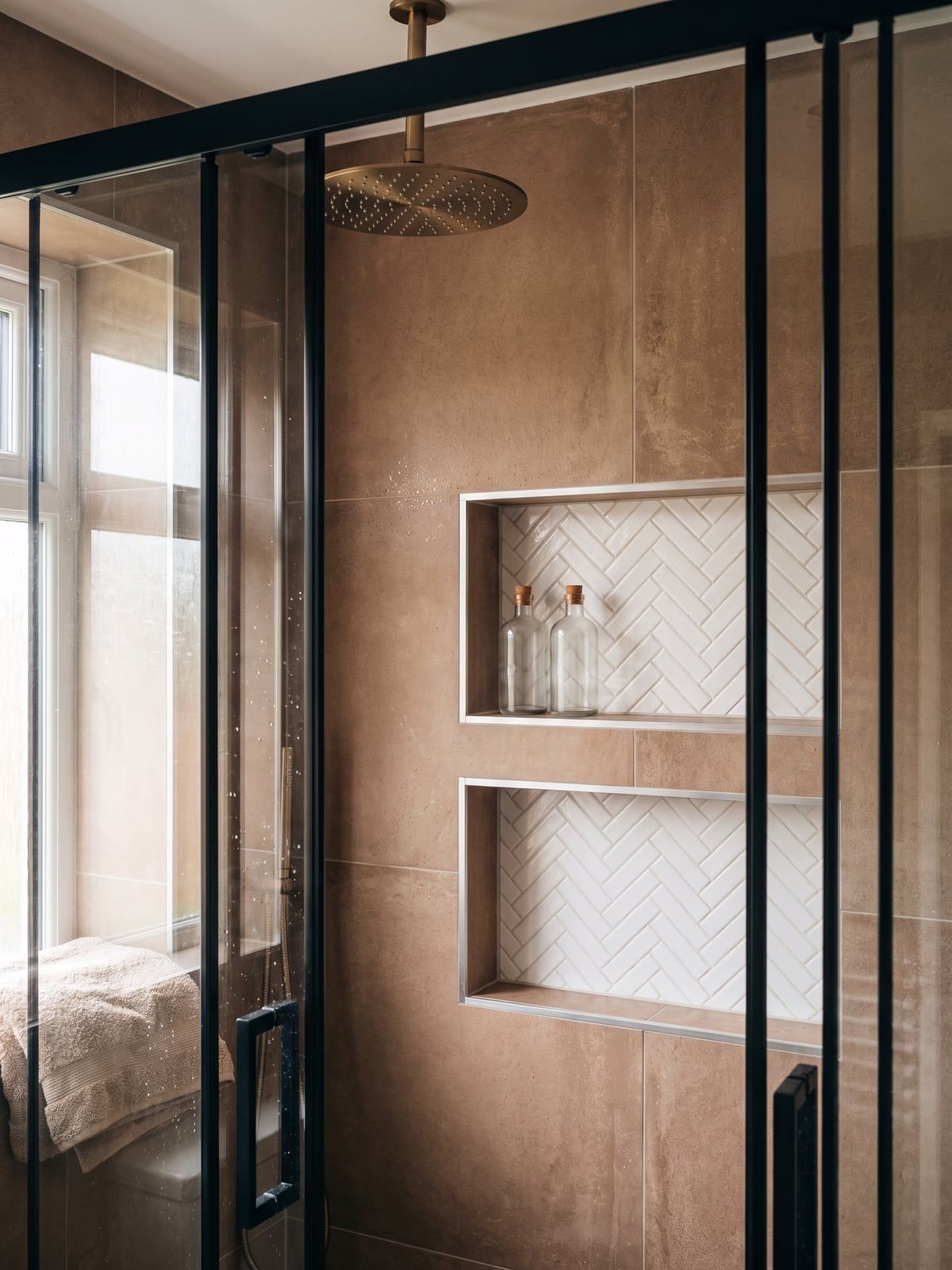 Shower with a brushed bronze rain shower at the top and two recesses lined in white herringbone tile