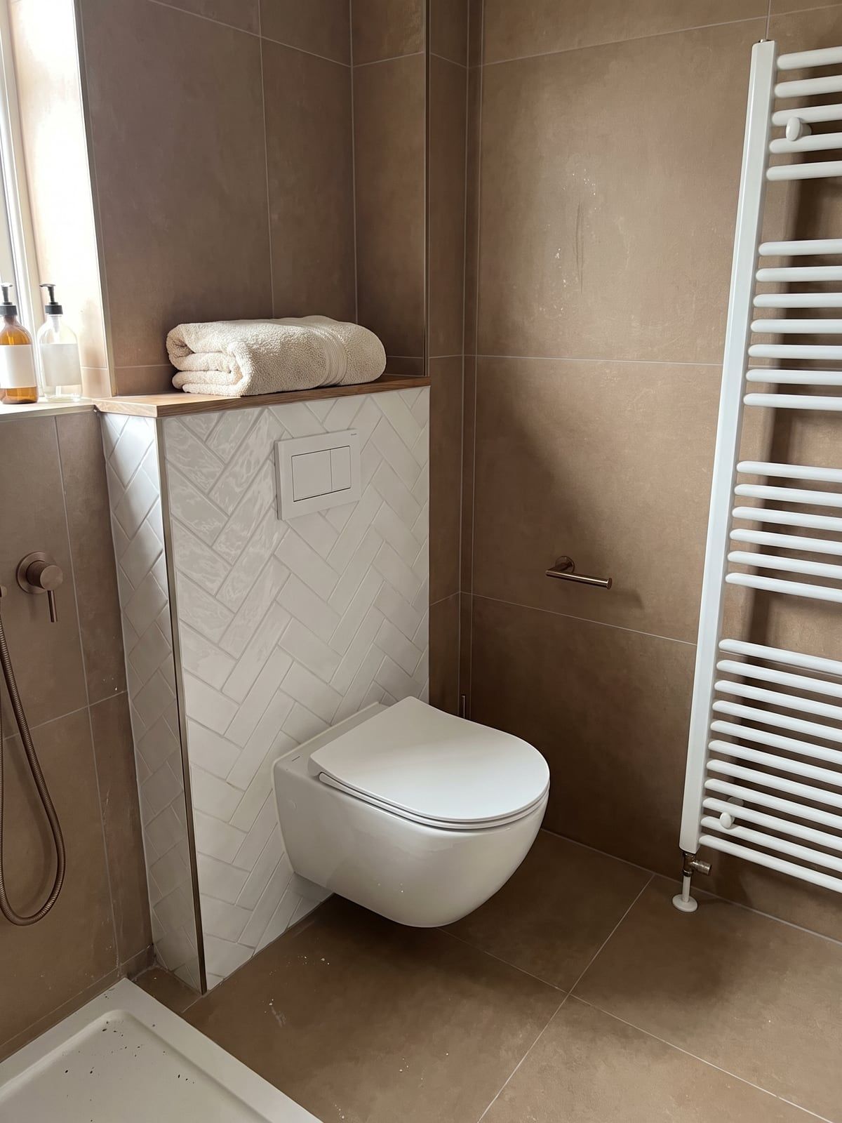 Wall-hung WC against a panel of white herringbone tile, with warm brown tiles beside it and a chrome flush plate